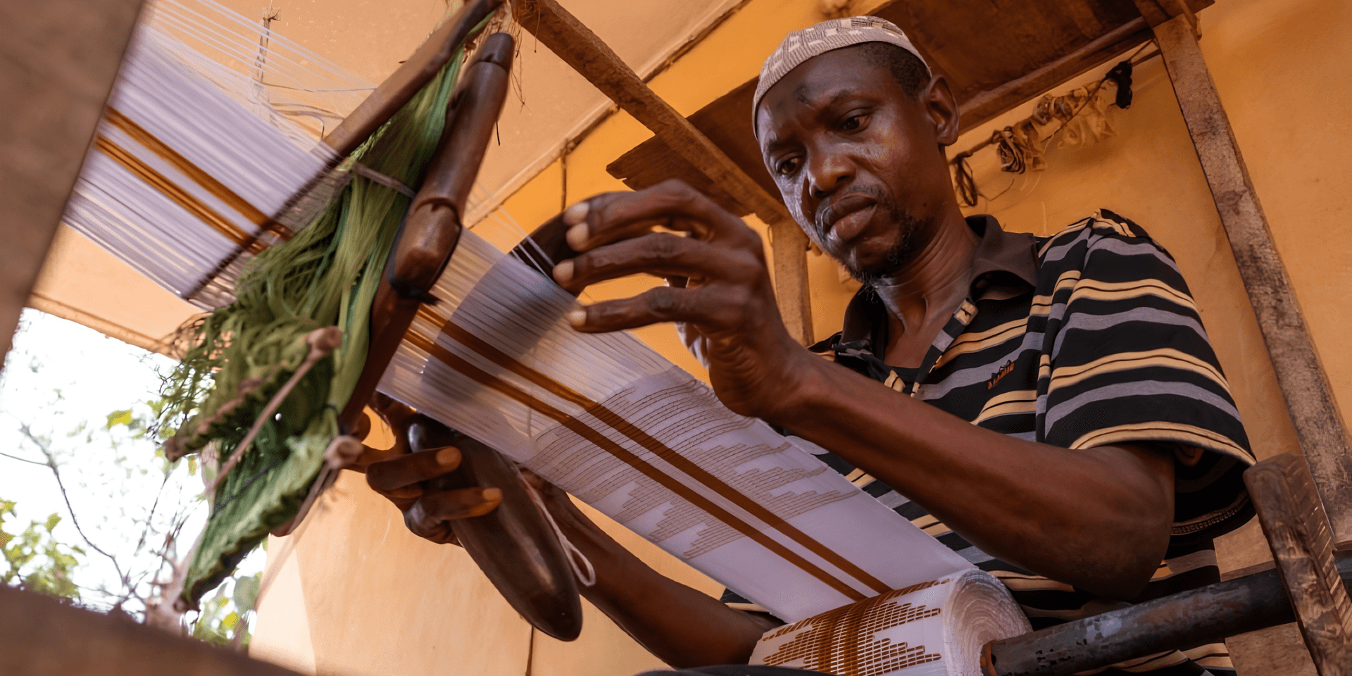 A man weaving fabric on a loom with focused concentration in a workshop