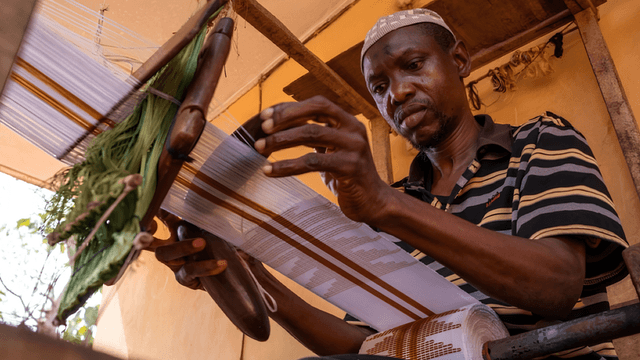 A man weaving fabric on a loom with focused concentration in a workshop