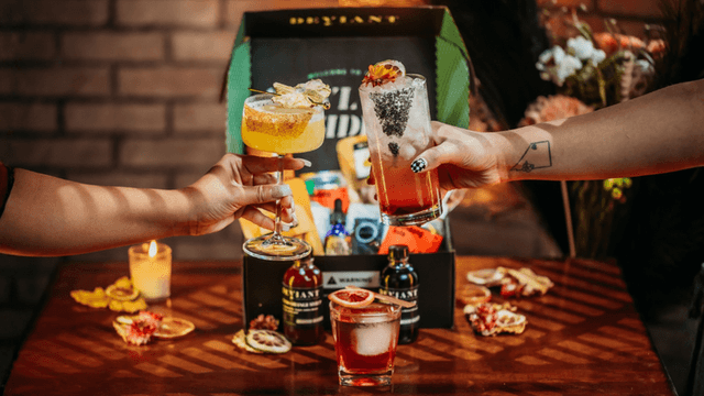 Three colorful cocktails being toasted with a gift box and decorative items in the background