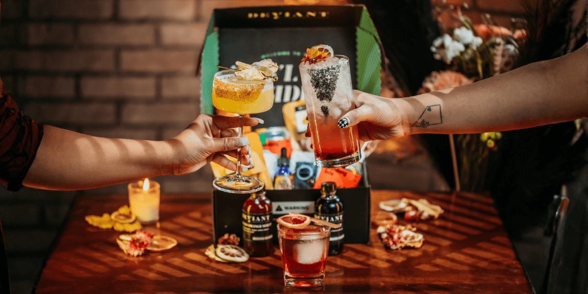Three colorful cocktails being toasted with a gift box and decorative items in the background