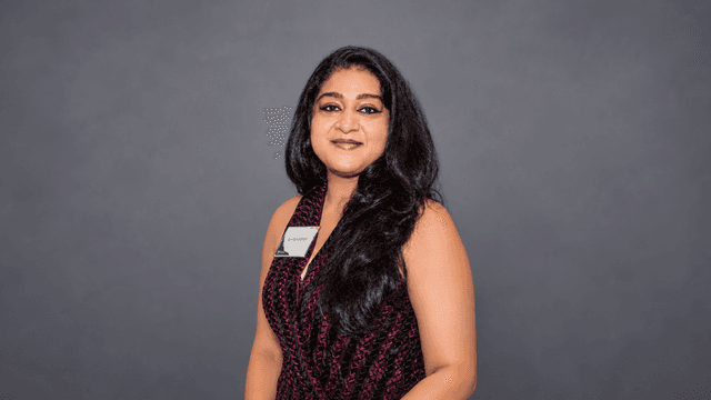 A woman with long black hair stands confidently against a gray backdrop