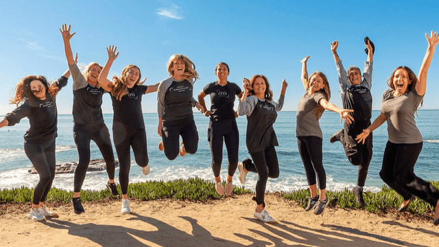 A group of eight people jumping joyfully by the ocean on a sunny day