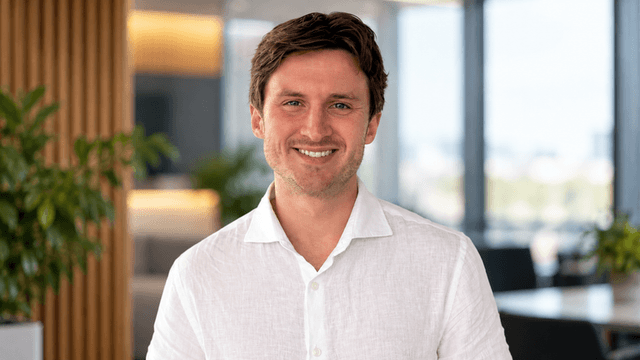 Smiling man in a white shirt standing in a modern office environment with plants.
