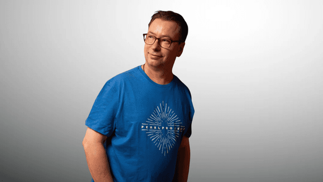 Man in a blue t-shirt stands confidently against a light gradient background