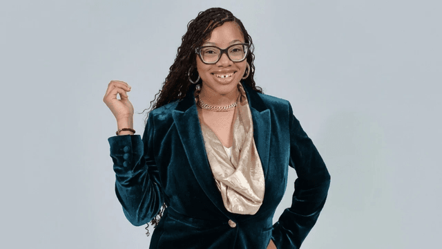 Woman in a teal velvet blazer and gold top smiling confidently at the camera