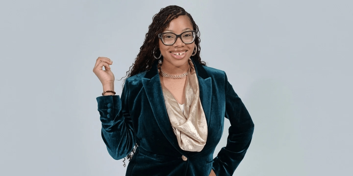 Woman in a teal velvet blazer and gold top smiling confidently at the camera