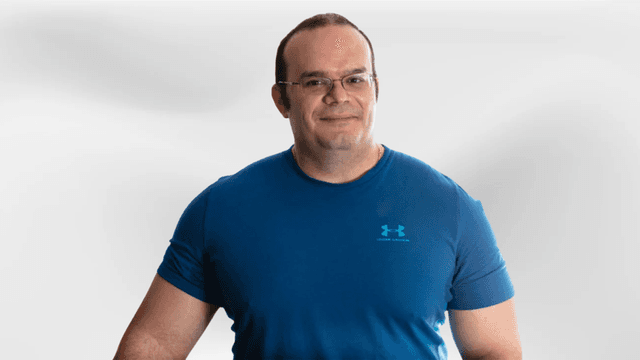 Man in a blue athletic shirt smiling against a light gray background