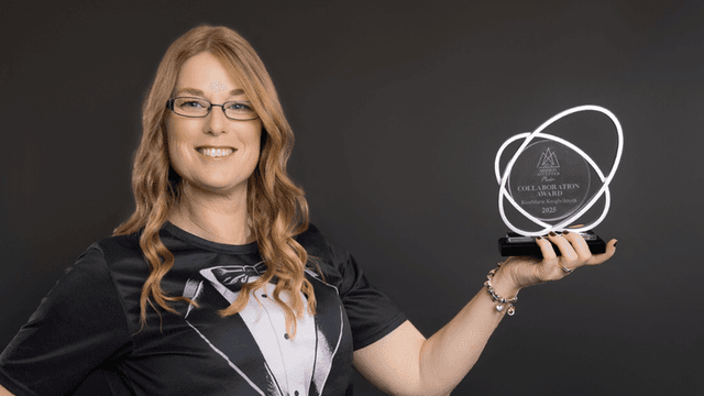 Woman in a tuxedo shirt holds an award in front of a dark background