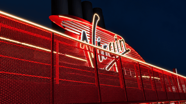 Illuminated Virgin logo on a red-themed structure against a dark sky
