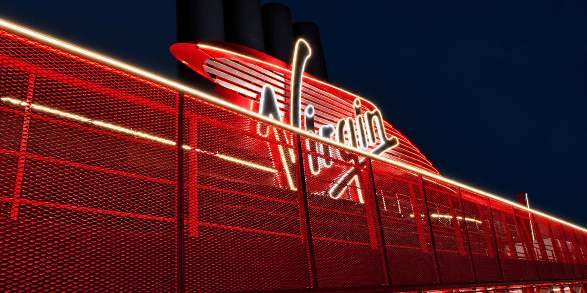Illuminated Virgin logo on a red-themed structure against a dark sky