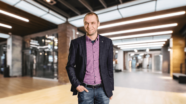 Smiling man in a blazer and striped shirt standing in a modern interior space