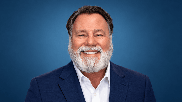 Smiling man with a beard, wearing a suit against a blue background