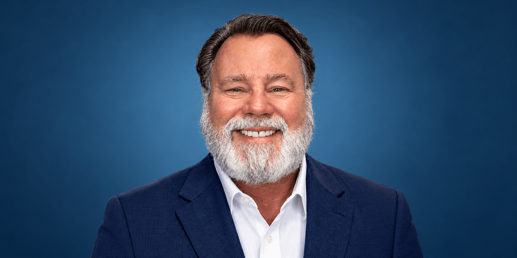 Smiling man with a beard, wearing a suit against a blue background