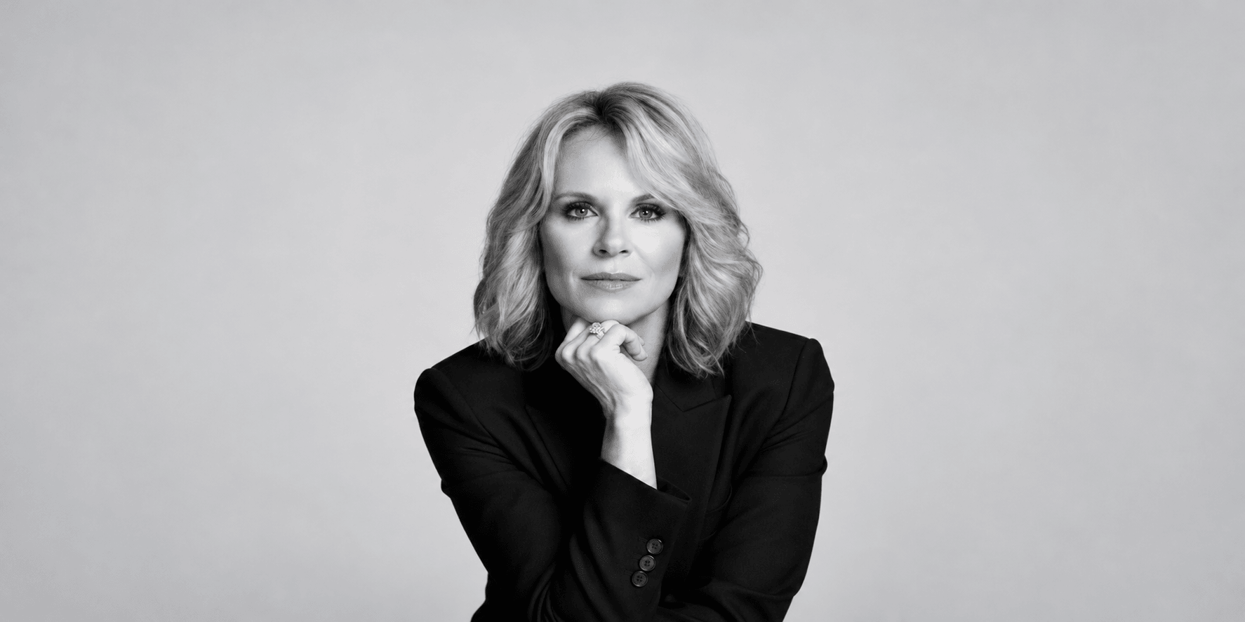 Black and white portrait of a woman in a blazer, resting her chin on hand