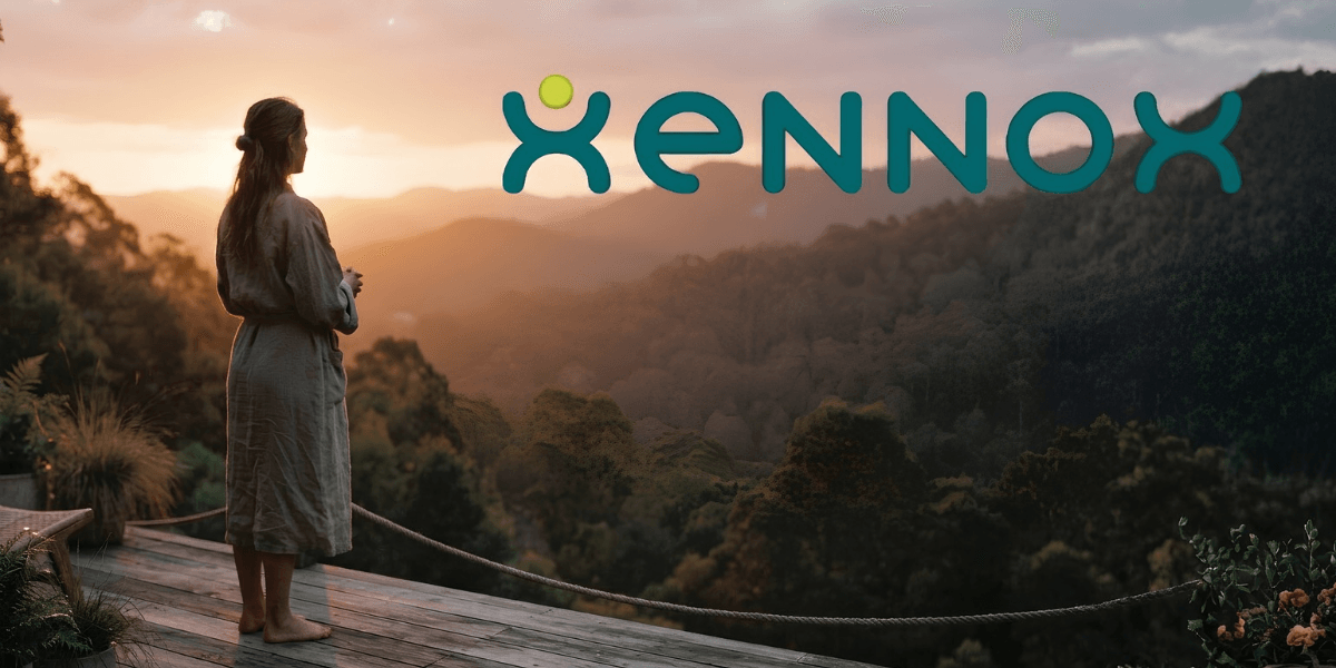 A woman stands on a deck, gazing at a scenic sunset landscape.