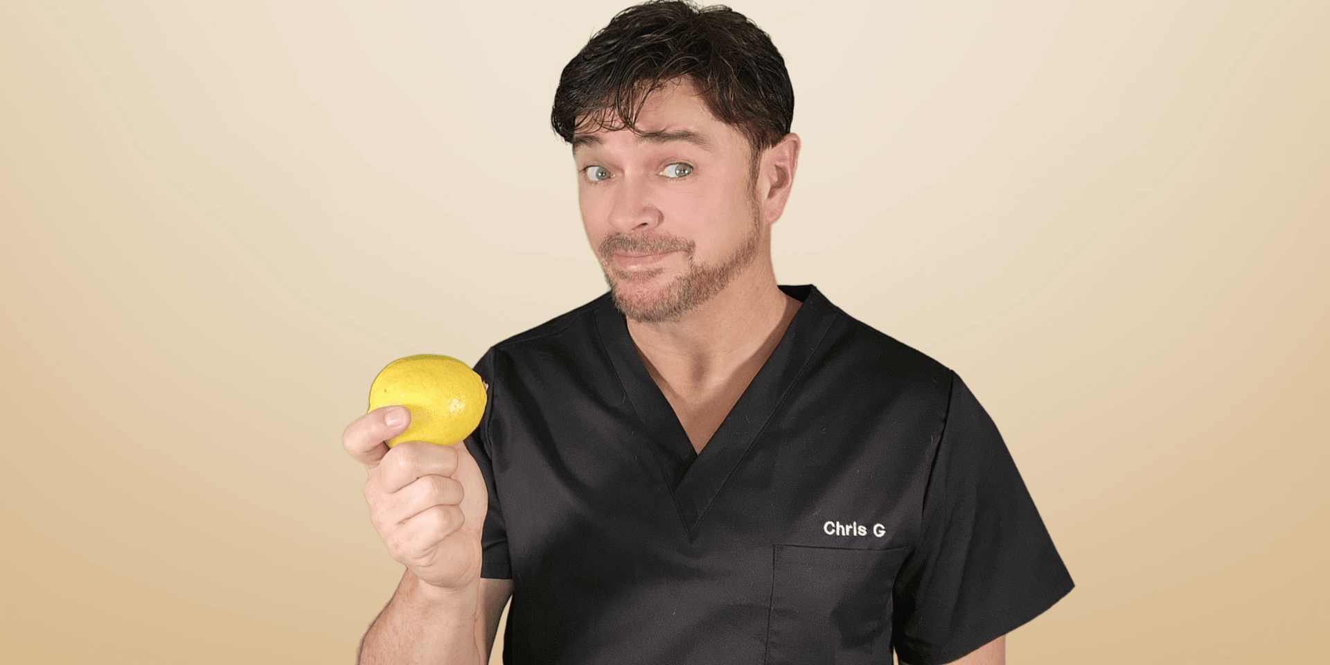 Man in a black medical scrub holds a lemon and smiles playfully