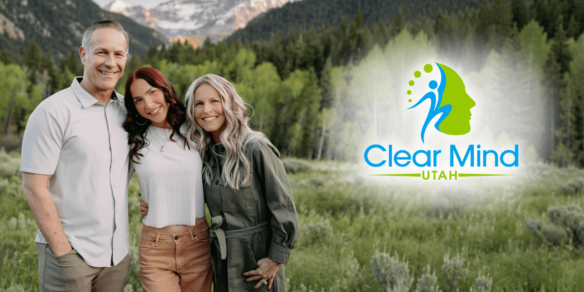 Three people smiling together outdoors with a mountain landscape and a logo overlay