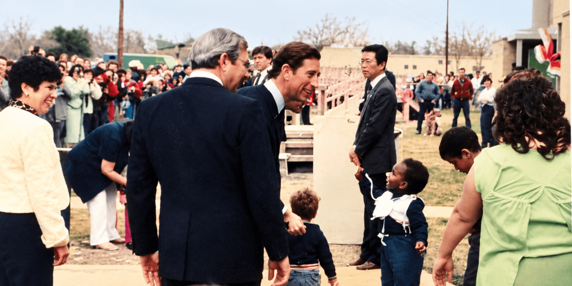 A gathering with people, including children, outdoors, smiling and interacting in a crowd.