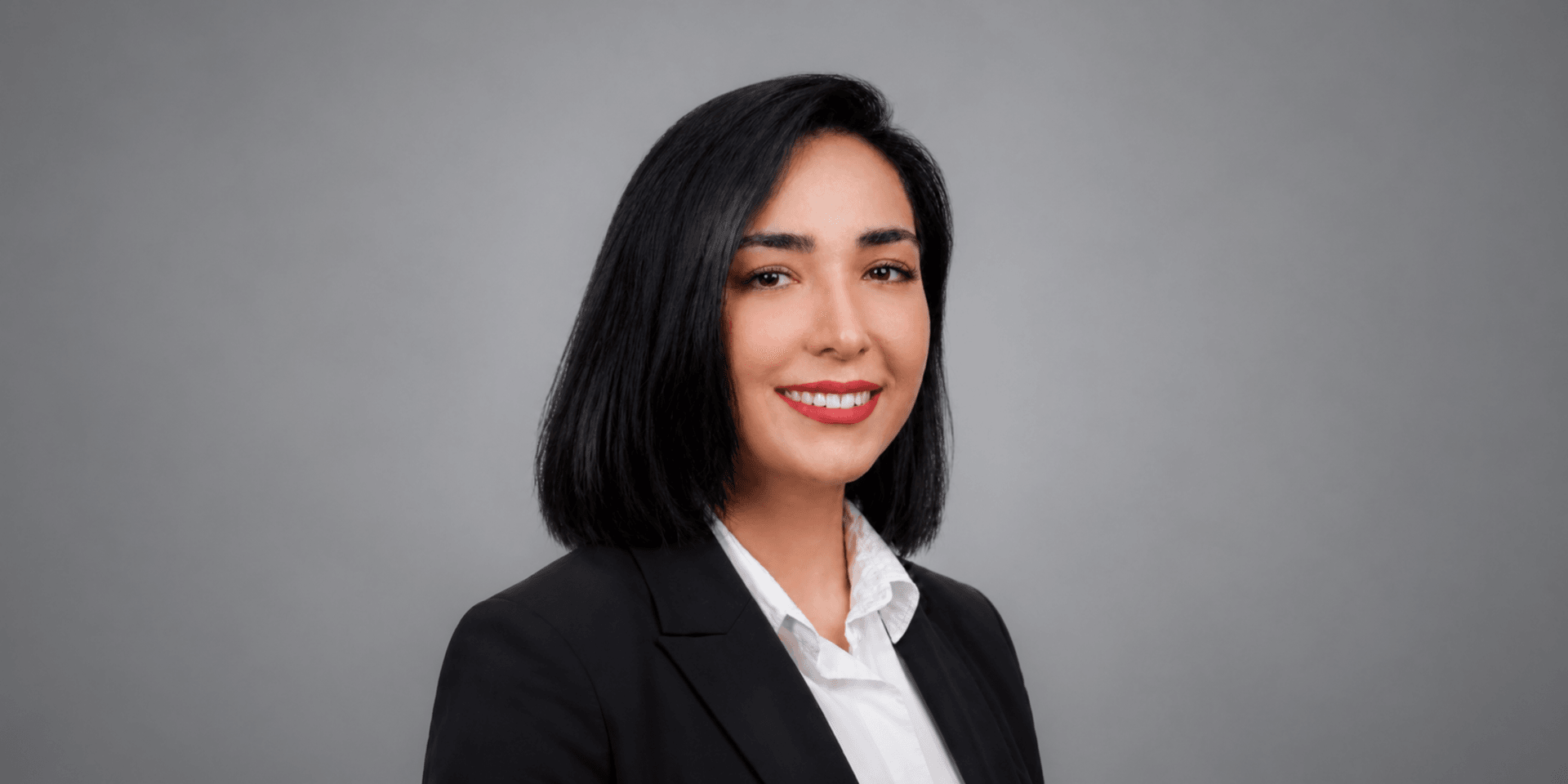 A professional woman with black hair wearing a dark suit and white shirt