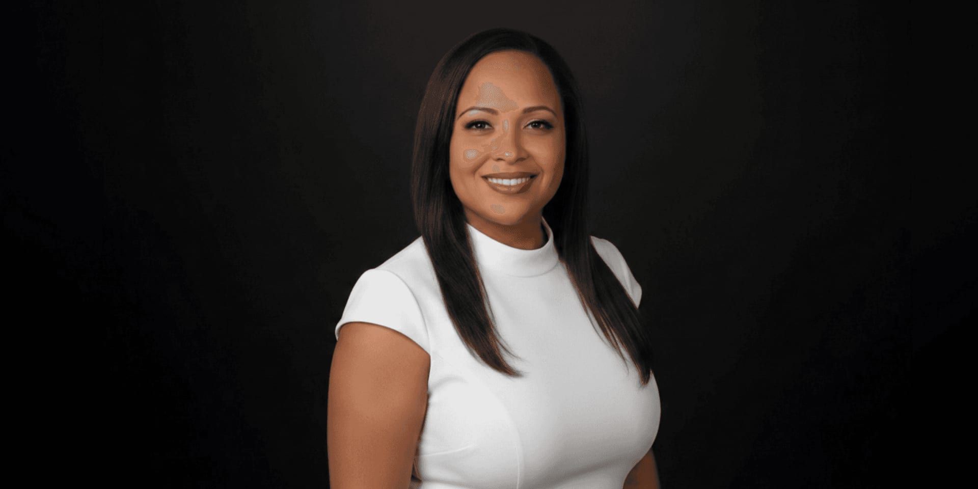 Professional portrait of smiling woman in white top against dark background.