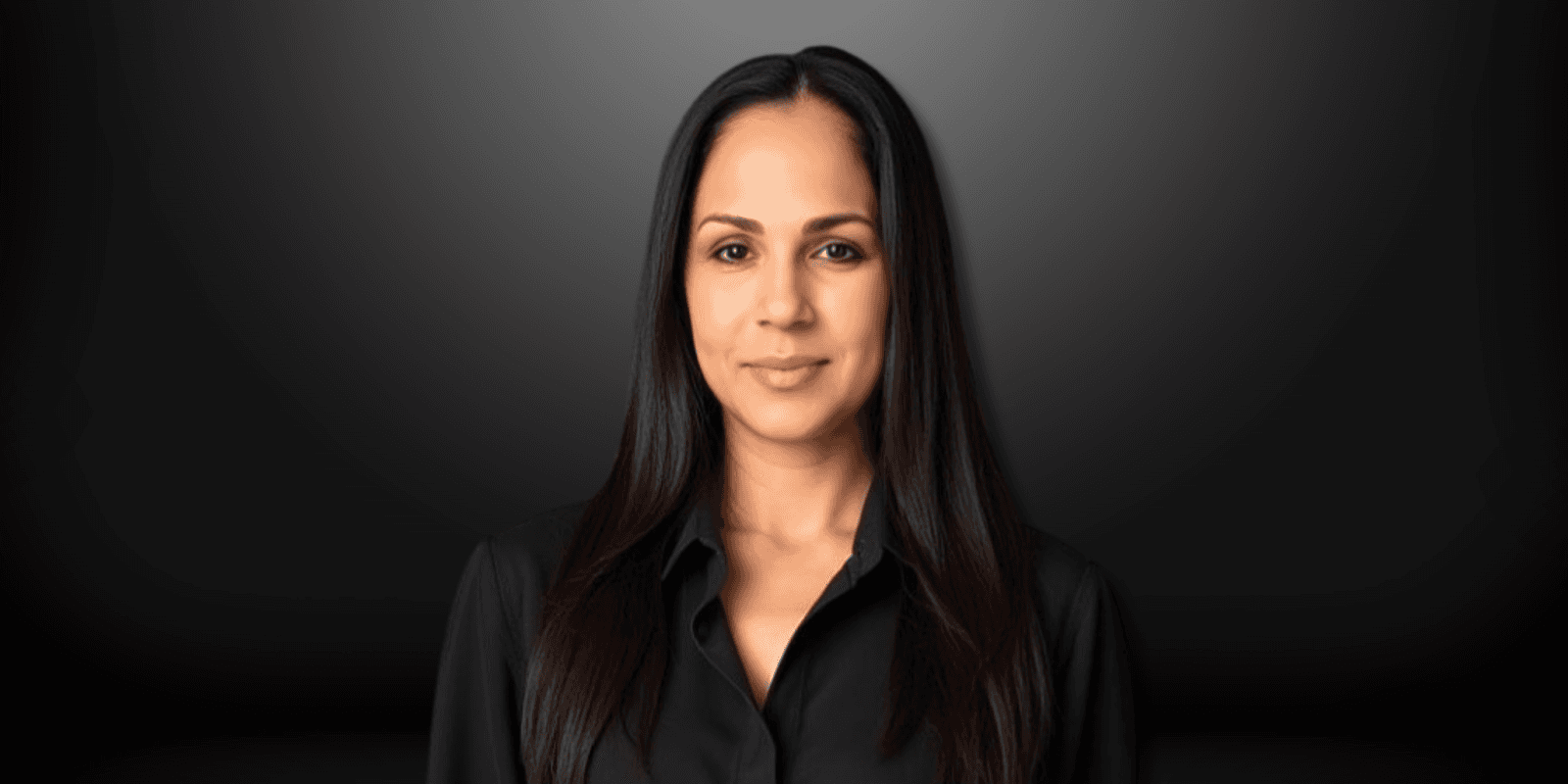 A professional headshot of a confident woman in a black shirt, with straight dark hair, standing against a simple black background.