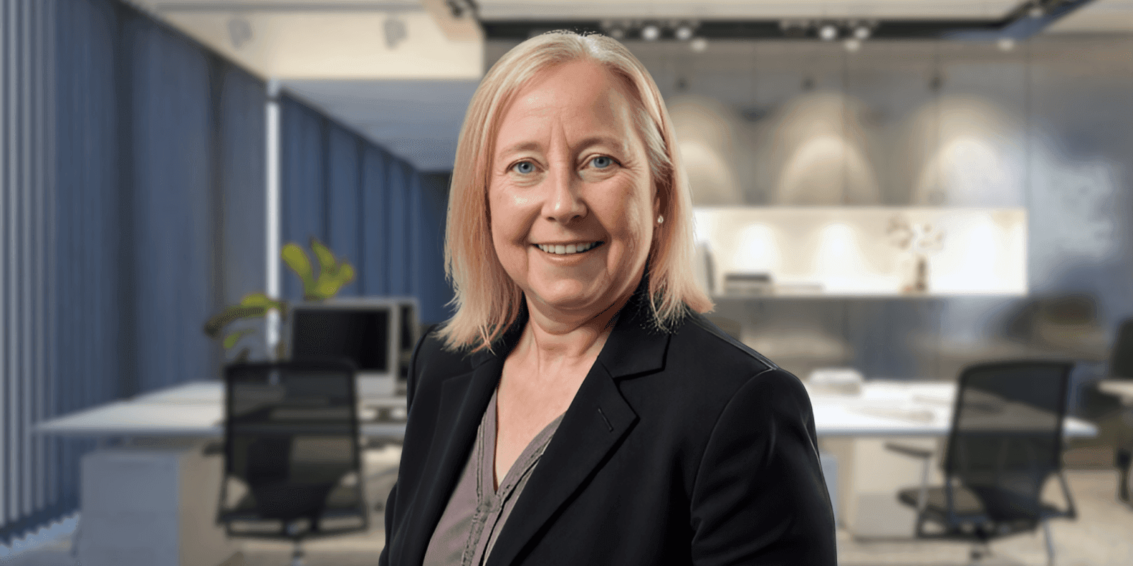 "A professional woman in a business suit smiles in an office setting with modern furnishings, exuding confidence and professionalism."