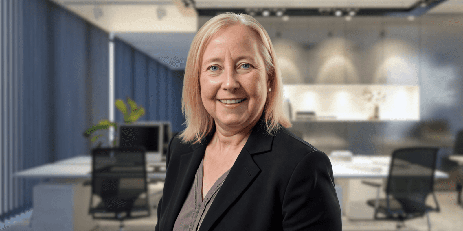 "A professional woman in a business suit smiles in an office setting with modern furnishings, exuding confidence and professionalism."