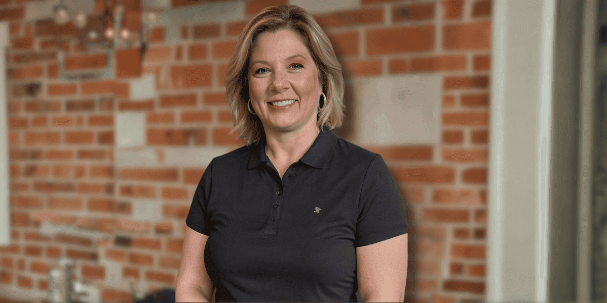 Penny Crook, CEO of Daneault, smiles in front of a brick wall, representing the innovative luxury handbag brand.