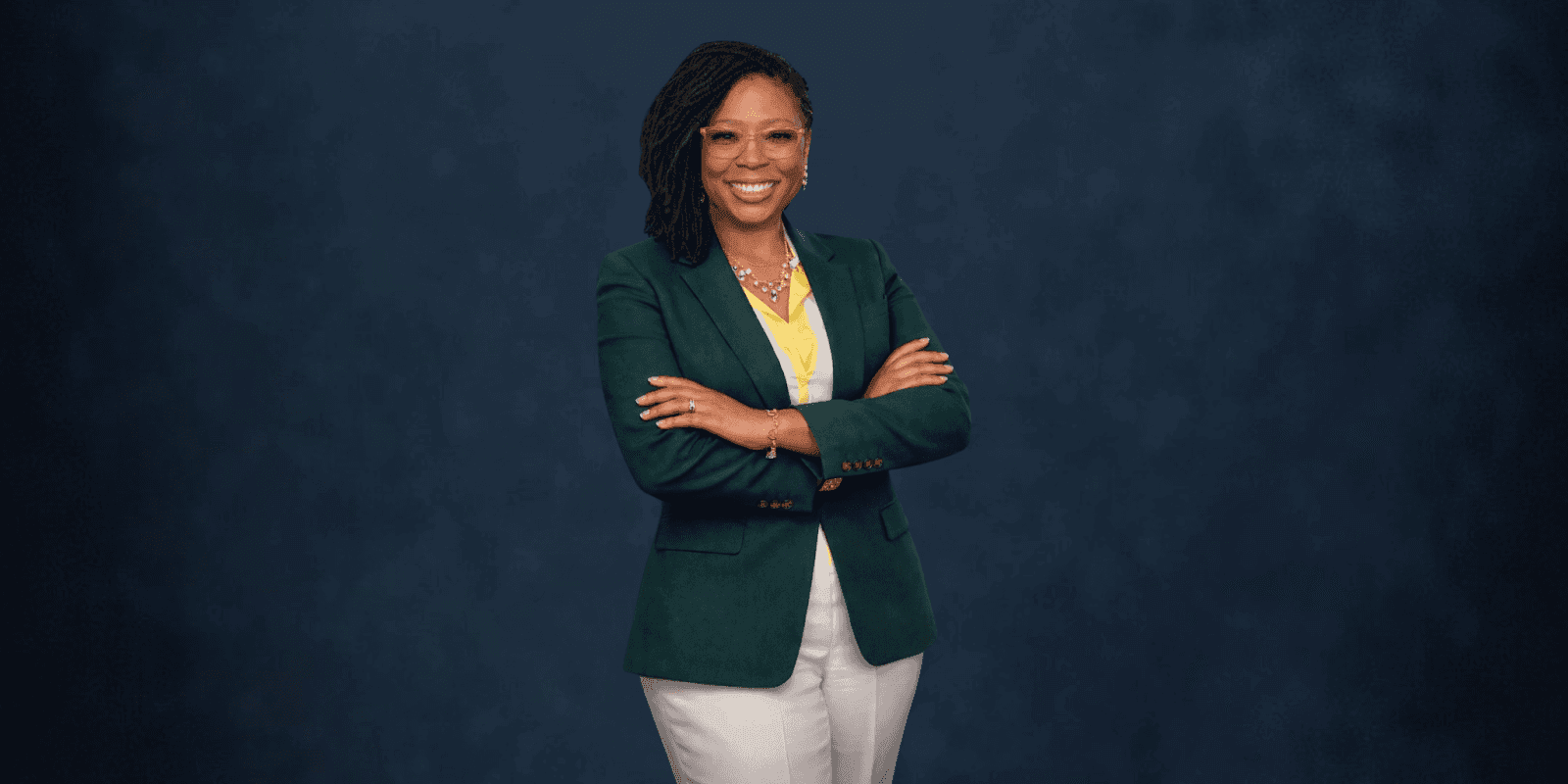 Shamicka C. Toney, an award-winning author and motivational speaker, standing confidently with arms crossed, wearing a green blazer and white pants.