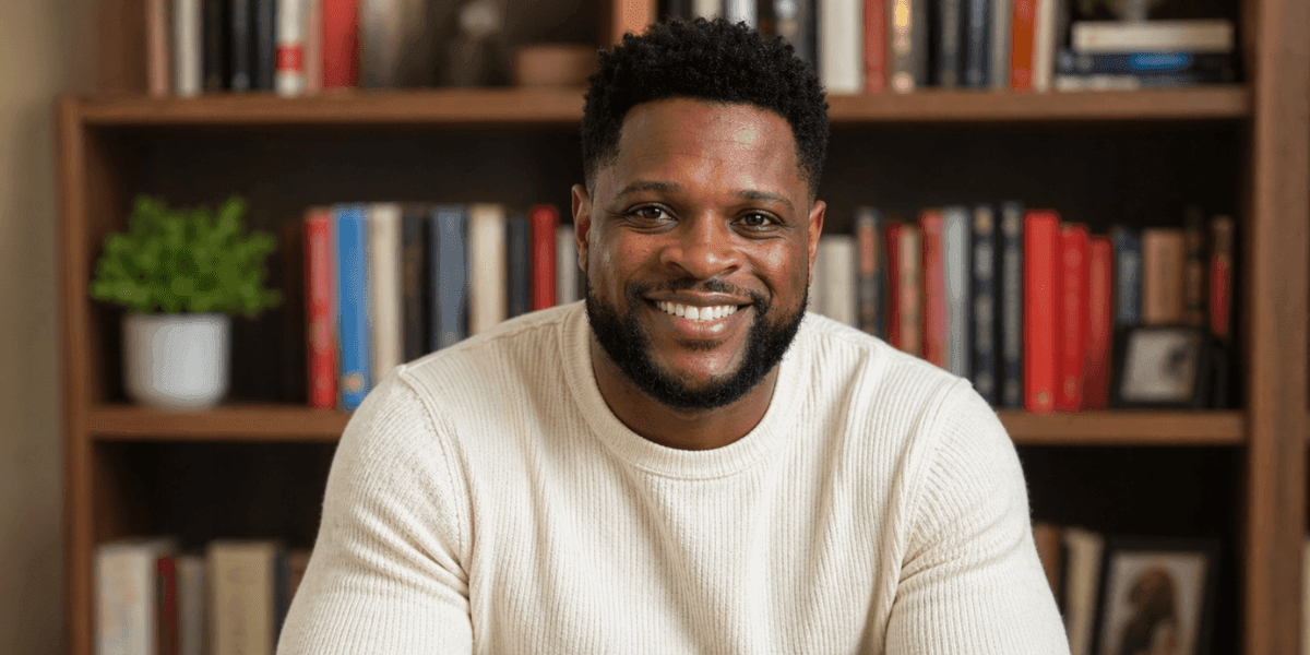 Author Michael Uboh smiling in front of a bookshelf while wearing a cream-colored sweater.