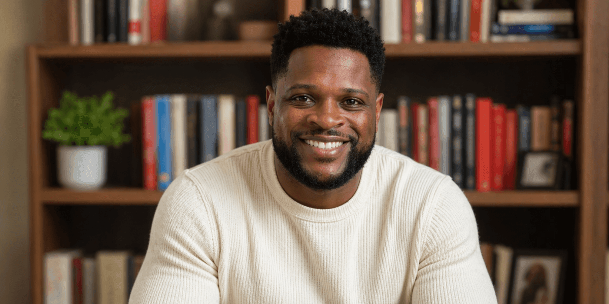 Author Michael Uboh smiling in front of a bookshelf while wearing a cream-colored sweater.