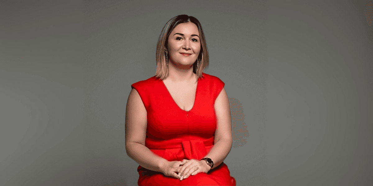 Professional portrait of a confident woman in a red dress, sitting against a neutral background, representing empowerment and leadership in a business setting.