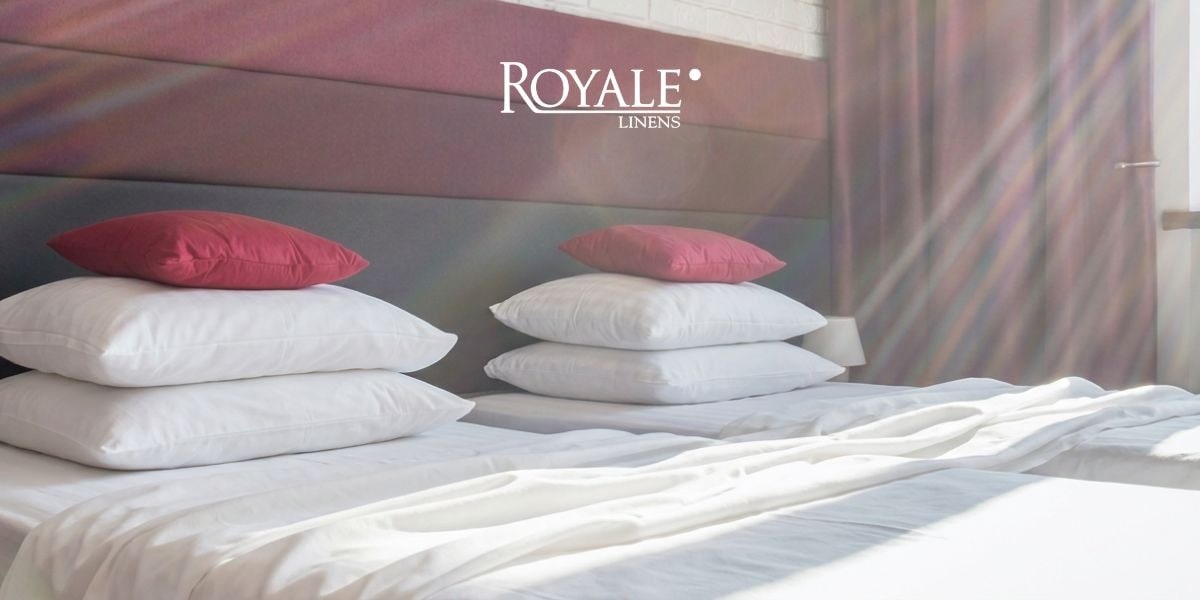 Neatly made bed with stacked pillows and white bedding from Royale Linens.