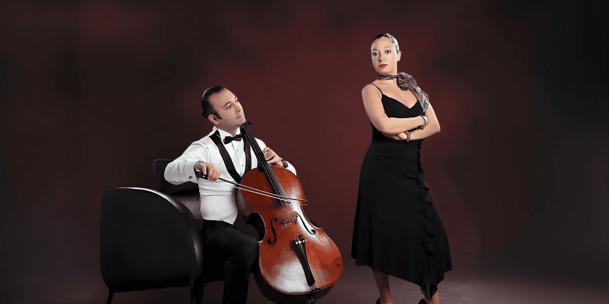 Man playing cello beside woman in black dress posing against a dark red background