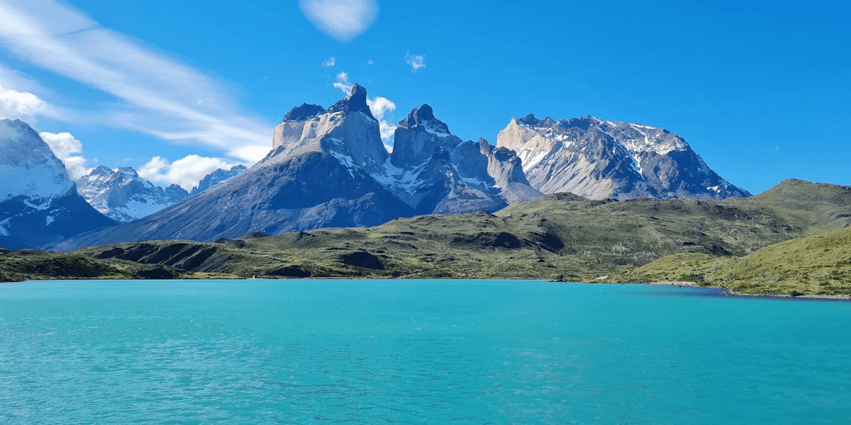 Turquoise lake with rugged snow-capped mountains under bright blue sky, scenic natural landscape.