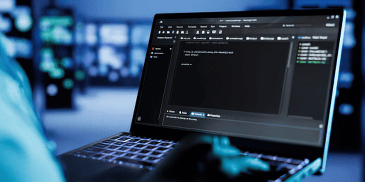 Person using a laptop displaying code in a dark interface, with blurred screens and a modern tech workspace background.