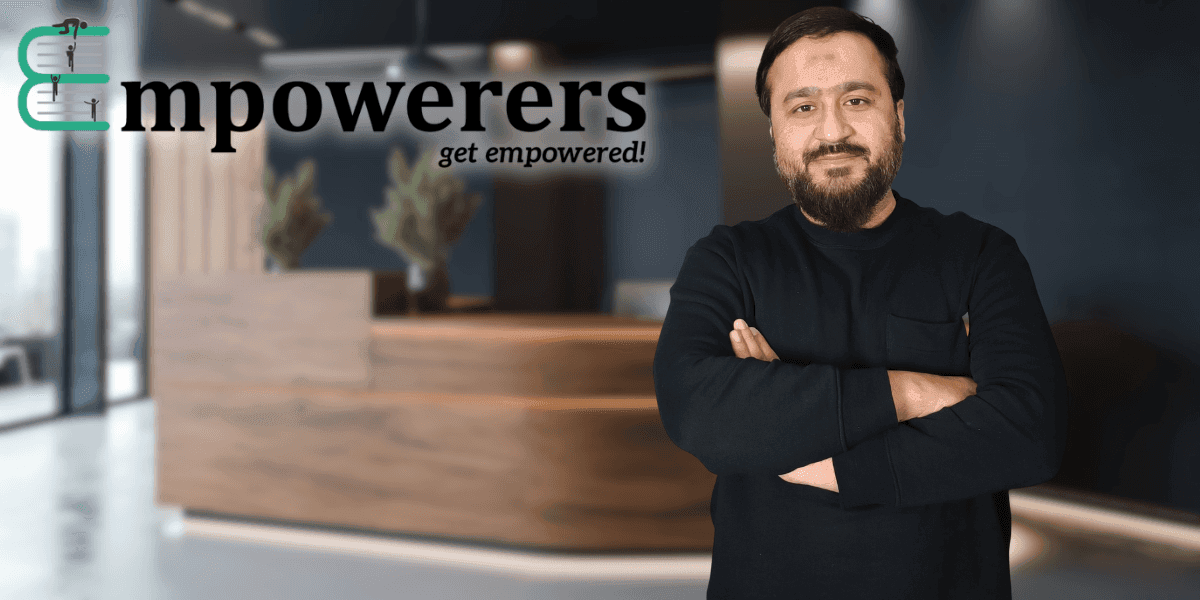 "Business owner or entrepreneur standing confidently with arms crossed, posing in front of a professional office space with Empowerers branding. The background features a modern workspace."