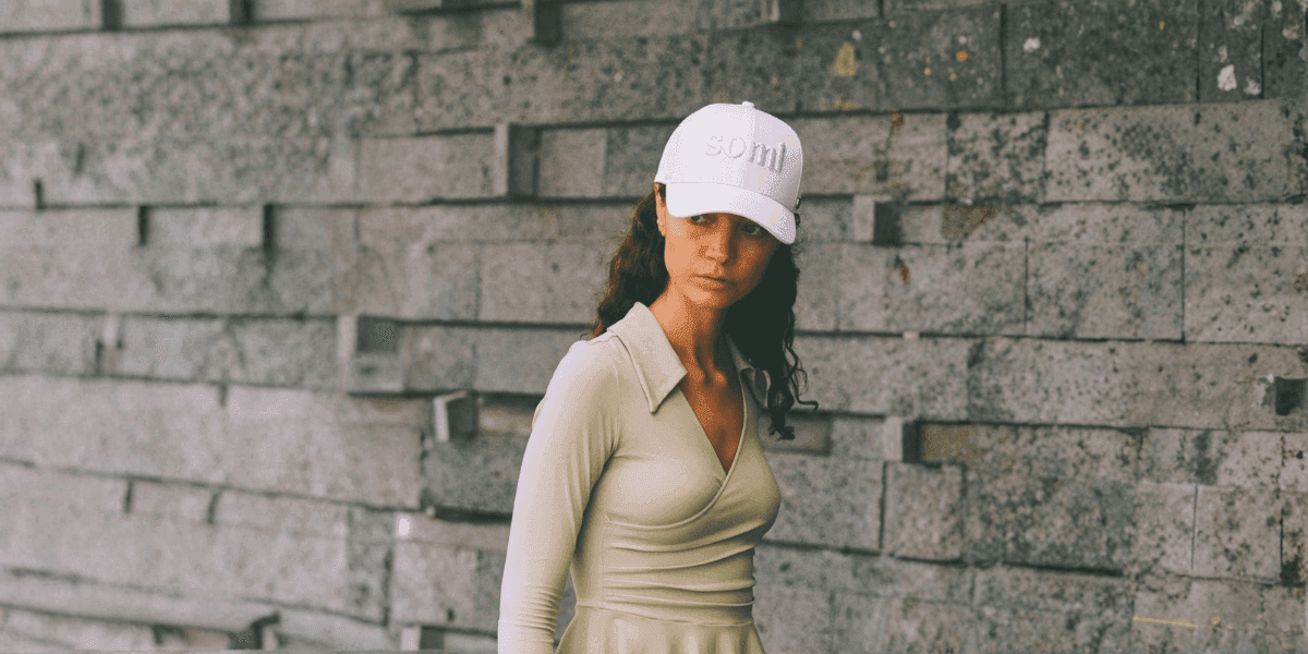 A modern explorer wearing a stylish white SOMI London cap, exuding elegance and adventure against a minimalist stone backdrop.