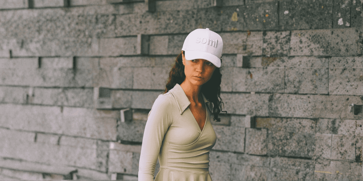 A modern explorer wearing a stylish white SOMI London cap, exuding elegance and adventure against a minimalist stone backdrop.