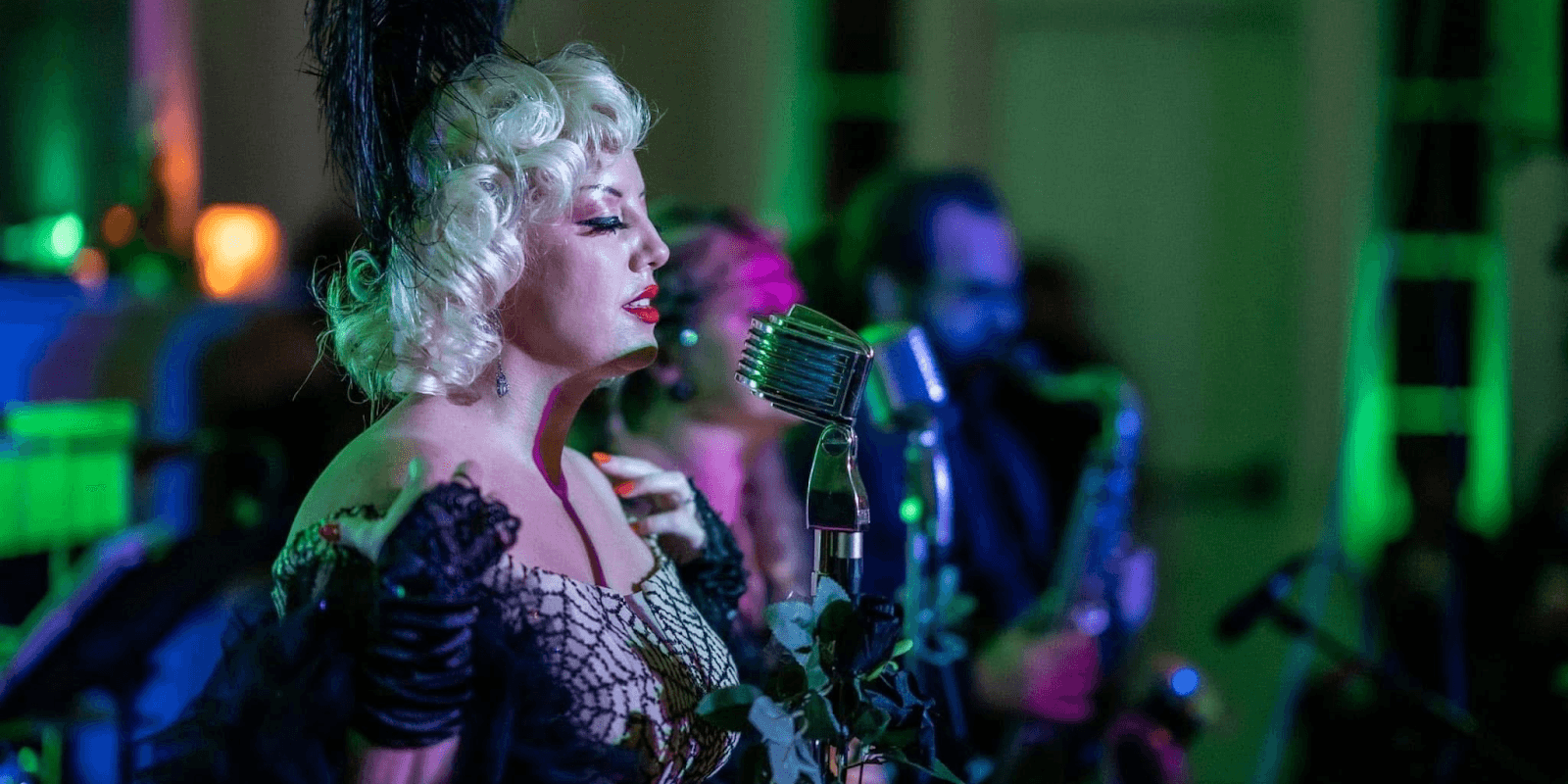 Vintage performer singing into a microphone at a haunted speakeasy event, surrounded by musicians in a spooky atmosphere.
