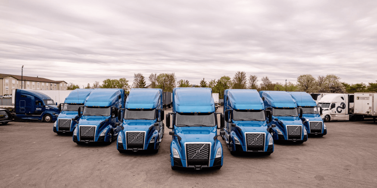 Fleet of blue semi-trucks parked together at a trucking company yard.