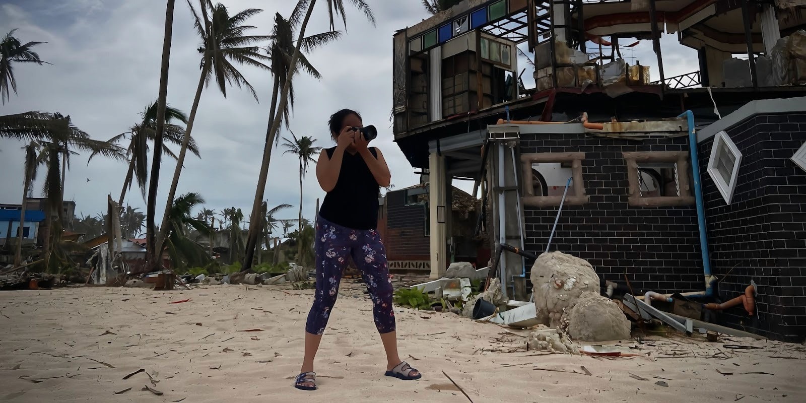 Woman photographing storm-damaged coastal area, capturing resilience and recovery, symbolizing Mandala Productions’ purpose-driven storytelling and humanitarian mission.
