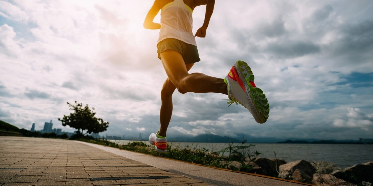 Runner sprinting along a waterfront path under dramatic clouds, showcasing speed, endurance, and outdoor fitness.