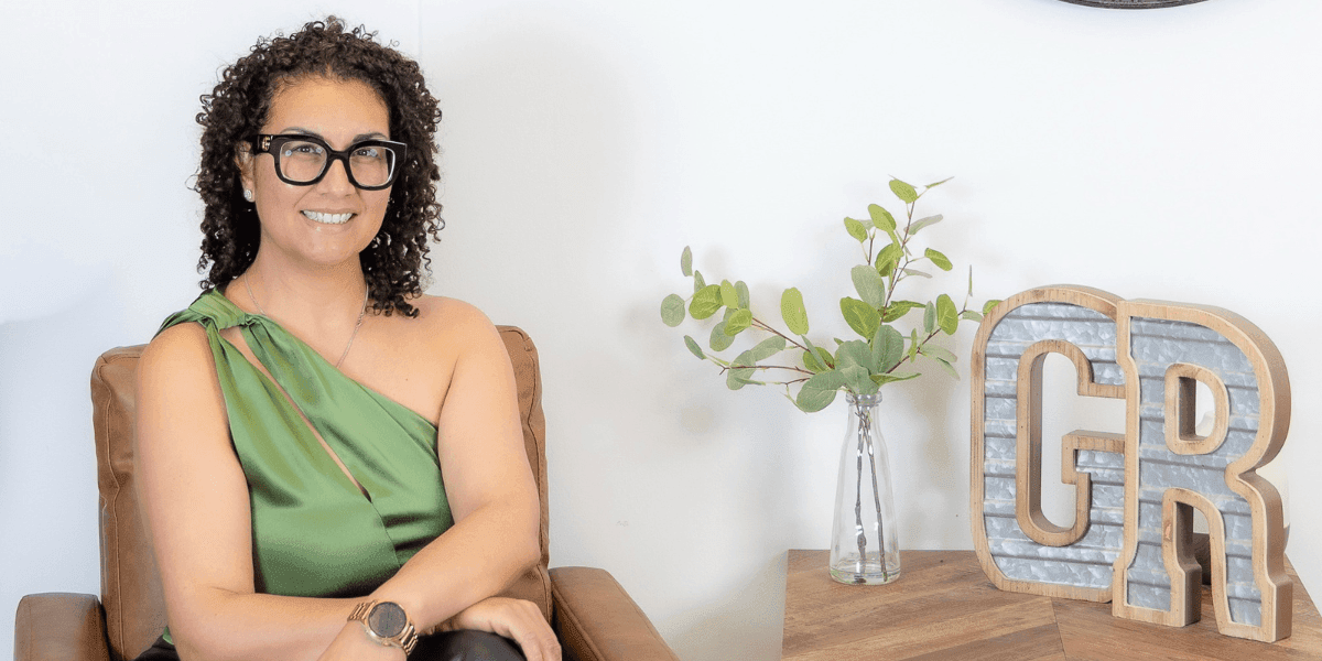 Portrait of mortgage broker Gina Reyes seated in office beside decorative initials and vase, smiling at camera.