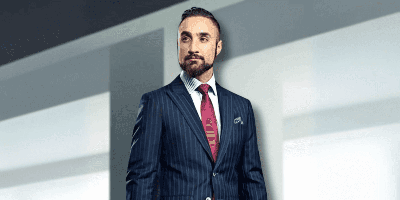 "Man dressed in a tailored navy pinstripe suit with a red tie and pocket square, standing confidently against a sleek, minimalist background, exuding professionalism and elegance."