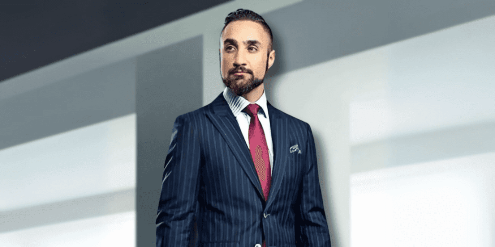 "Man dressed in a tailored navy pinstripe suit with a red tie and pocket square, standing confidently against a sleek, minimalist background, exuding professionalism and elegance."