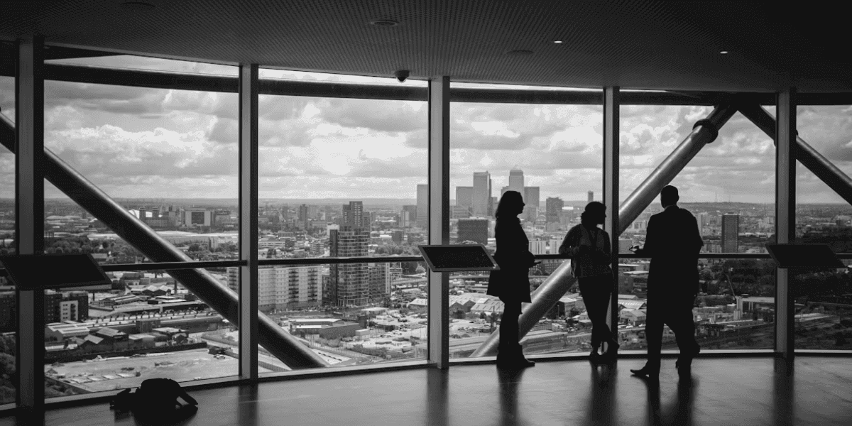 Silhouetted professionals discussing inside office with panoramic city skyline view through large windows.
