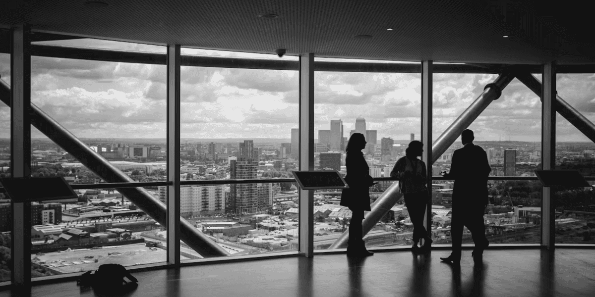Silhouetted professionals discussing inside office with panoramic city skyline view through large windows.