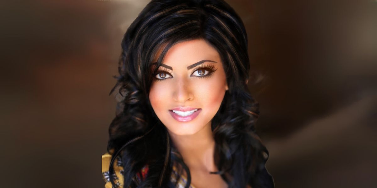 Close-up portrait of a woman with dark, voluminous hair and stunning brown eyes, wearing a colorful scarf and smiling confidently.