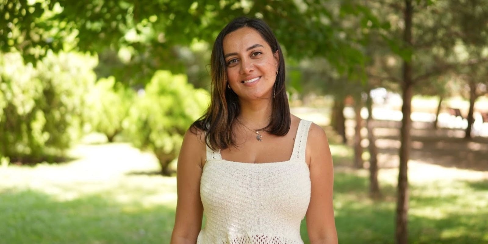 Gunay Rasulova, founder of You Will Speak, smiling outdoors in a white dress with a nature background.